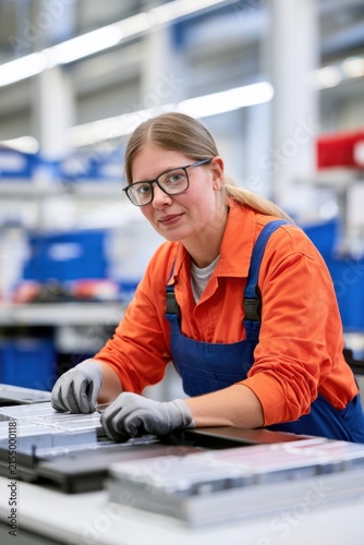 Female factory assembler in orange coveralls working on electronic parts on production line for industrial brochure and website background
