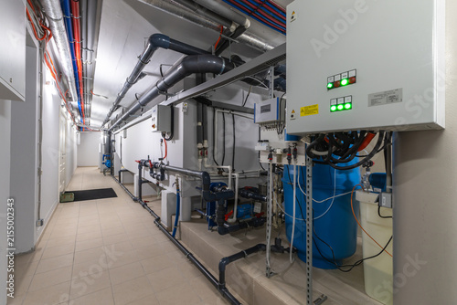 The scene shows a technology room with various pipes, valves, and control panels. The setting is inside a building, focusing on equipment for heating and cooling