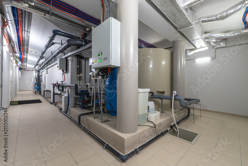 Water treatment equipment and plumbing inside a building. It has tanks and pipes arranged in a neat way. The area has bright lighting