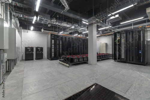 Inside a data center, several server racks are arranged along the walls. Equipment is stored on the floor. The setting has bright lighting and a clean layout
