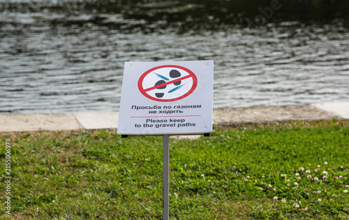 Sign on lawn with Russian text keep off the grass. Warning notice on urban embankment grassy area. Public park rule signage