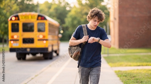 Young student checking the time on his watch while walking away from a yellow school bus on a sunny afternoon, symbolizing the transition from school to home.