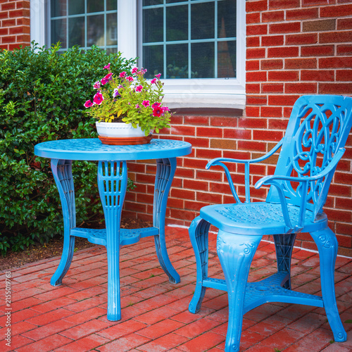 Bild auf Leinwand Blue metal bench and table with vase of flowers in the front yard