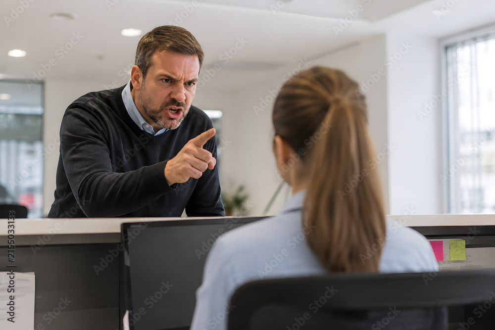 Fototapeta premium Angry customer pointing at a stressed office employee during a heated verbal confrontation, capturing workplace harassment, customer aggression and professional conflict.