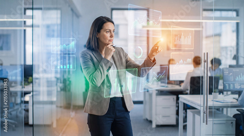 Thoughtful businesswoman interacting with financial chart projection office, focused professional analyzing digital data with intense expression