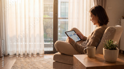 Focused young woman reviewing portfolio on tablet in comfortable home, feeling calm and productive while sitting in sunny living room