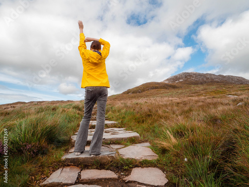 Cuadro en lienzo Girl tourist in yellow jacket is standing on a stone footpath leading to The Diamond hill in Connemara National park, county Galway, Ireland