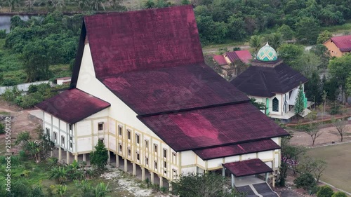 A large traditional Banjar house with a red roof sits amidst trees and grass, south Kalimantan