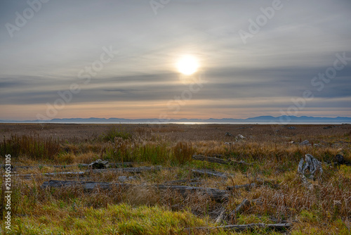 Sunset over a wide field with sun setting behind distant mountains near a lake