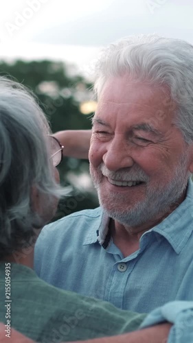 Elderly caucasian couple with gray hair hugging tenderly in a park at sunset, showing affection and love. A hot air balloon is visible in the background, adding a touch of romance and dreaminess