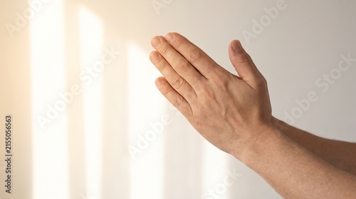 Hands in prayer, bathed in soft, warm light with vertical shadows on a light background. A symbol of devotion and hope