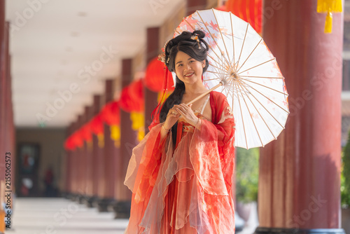 Cuadro en lienzo Portrait of an elegant young woman in traditional red Chinese hanfu: parasol tilted further, bigger smile, framed by red pillared corridor, in a cultural portrait of classical Chinese dress