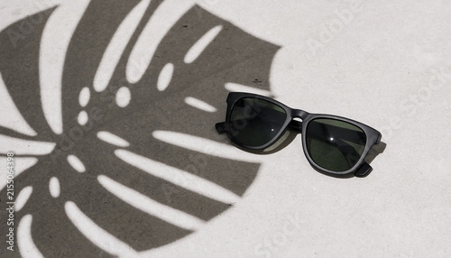 Stylish sunglasses with shadows on a light surface