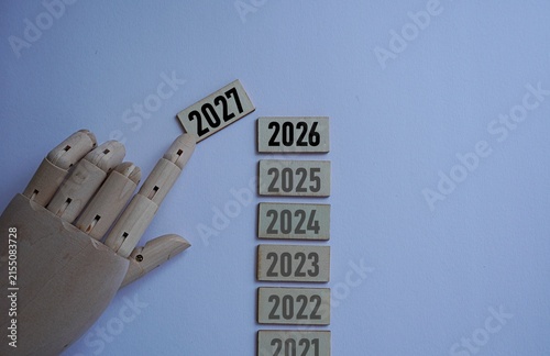 Replica wooden hand pushing in printed wooden pieces 2027 on top of the previous year's arrangement. New year celebration concept. Joy of the year's transition. Celebrating public holidays