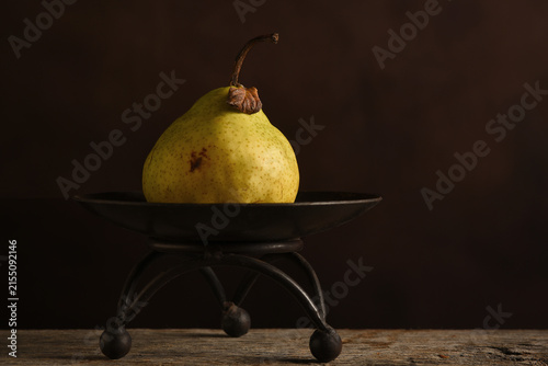 Fruit Still Life. An Anjou Pear on a pedestal against a warm brown mottled background.