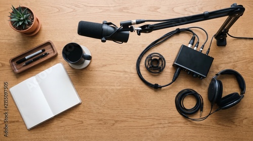 Podcast Studio Setup: A professional podcasting setup on a wooden desk, featuring a condenser microphone, headphones, audio interface, and notepad, ready for recording.