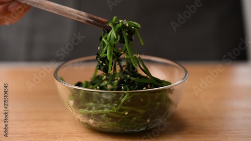 Hand using chopsticks to eating Korean spinach salad (Segeumchi namul) in a bowl