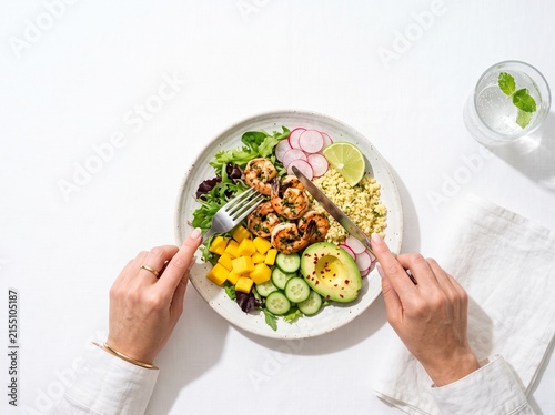 Person eating fresh shrimp salad with avocado and mango on white plate.