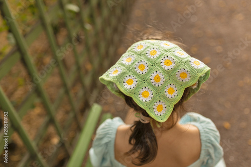 Little girl wearing green crochet daisy bandana or headscarf, view from the back