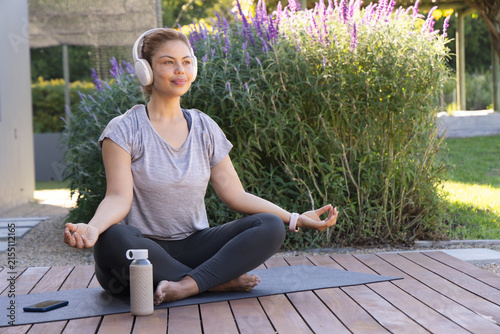 African American woman meditating on deck mat, wearing grey tee and black leggings with headphones