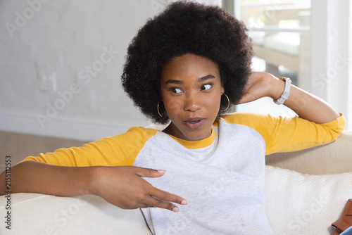 Photography African teenage woman sitting on light sofa at home wearing hoop earrings and wr