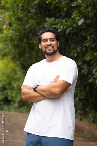 African-American man standing on path by hedge, in white tee and blue shorts, smartwatch, smiling