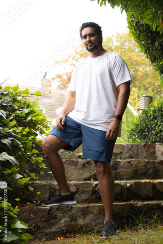 African American man standing on stone steps in garden wearing white T-shirt and wristwatch