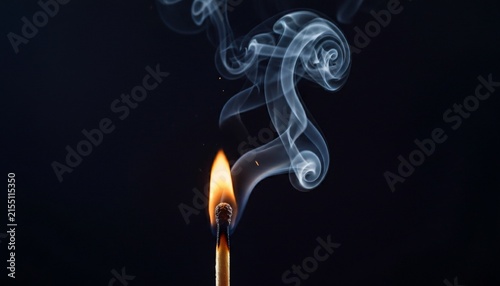 A single burning matchstick creating wisps of smoke against a dark background.