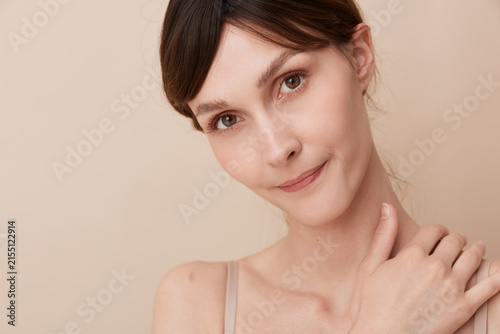Fotografía A calm woman portrait with soft lighting, clear skin, and serene expression against a neutral beige background, conveying simple natural beauty and poise