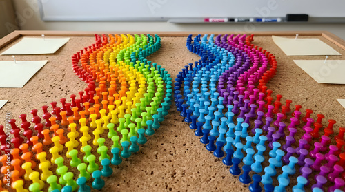 Rainbow heart shape made of colorful push pins on cork board