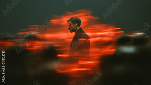 Loneliness and Anxiety Concept with Man Standing Still Among Blurred Crowd Under Red Light