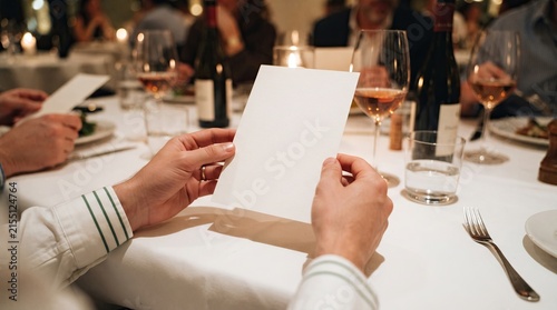 A person holding a blank white menu card at a formal dinner party with blurred restaurant background