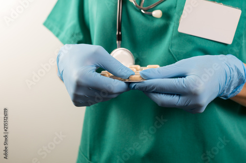 Canvastavla Torso shot of a healthcare worker wearing green scrubs and blue nitrile gloves, holding and examining a foil blister pack containing round beige medication tablets