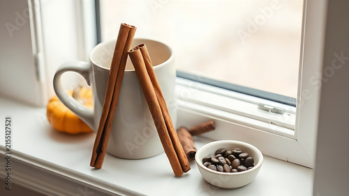 Fall beverage still life with cinnamon sticks, coffee mug, coffee beans, mini pumpkin on window ledge