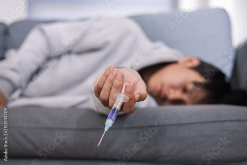 Man Unconscious on Sofa Holding Syringe After Drug Overdose, Focusing on Needle in His Head