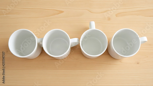 Four identical white ceramic mugs lined up in a row on minimalist wooden table.