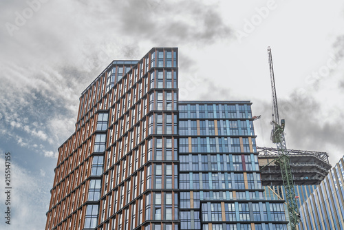 View of modern high-rise buildings with glass and metal facades and a construction crane against a cloudy sky in London, England, United Kingdom.