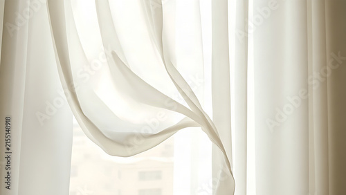 A soft white curtain billowing in a breeze against a sunlit window, forming smooth, wave-like folds.