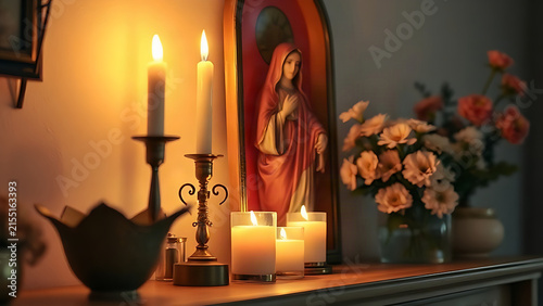 Home altar with flickering candlelight illuminating religious statue and fresh flowers.