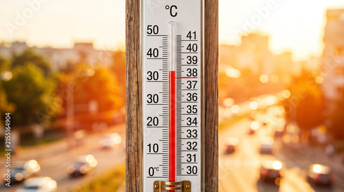 Outdoor thermometer showing high temperatures during a summer heatwave in an urban setting.