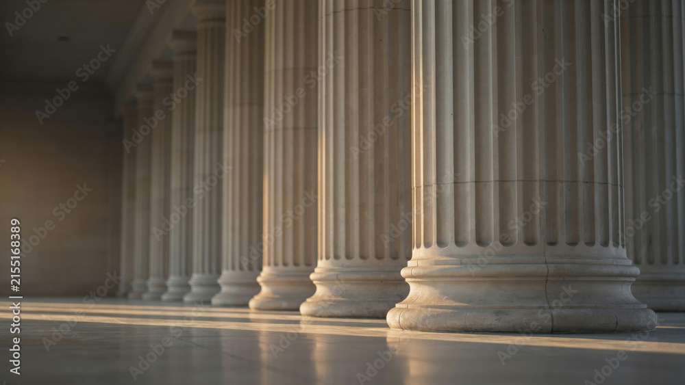 Fototapeta premium Row of classical stone columns on public building exterior with morning sunlight and long shadows
