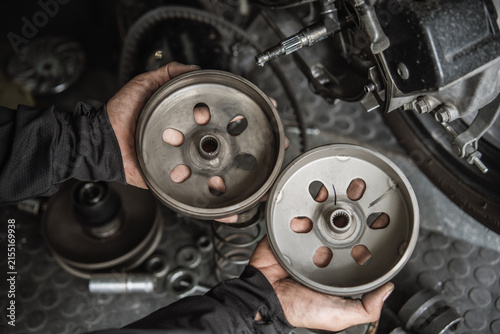 Mechanic hands holding motorcycle clutch bells for inspection during CVT transmission repair