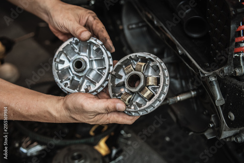 Mechanic hands holding motorcycle CVT variator pulley and roller weights during transmission inspection