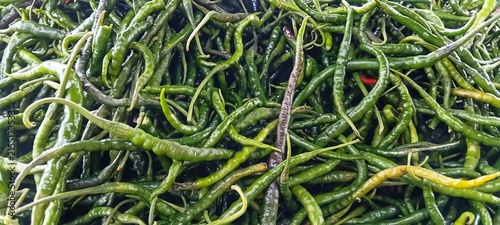 Foto Group of fresh harvested green hot chilies stacked on display at an open air mar