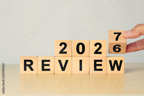Hand flips wooden cube from 2026 to 2027 over REVIEW word, showing end of year summary and future planning