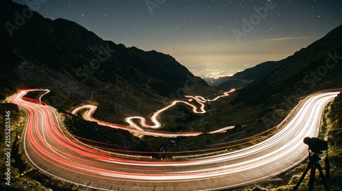 Long exposure photograph of car light trails on a winding mountain road at night, showcasing dynamic movement.