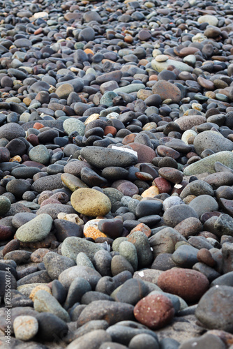 Close-up of natural wet pebbles and smooth river rocks on a beach shore, creating a textured surface polished by water and waves.