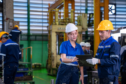 Team of industrial worker is checking the setup value of  metal casting machine by automated monitor while working inside roof factory for safety industry