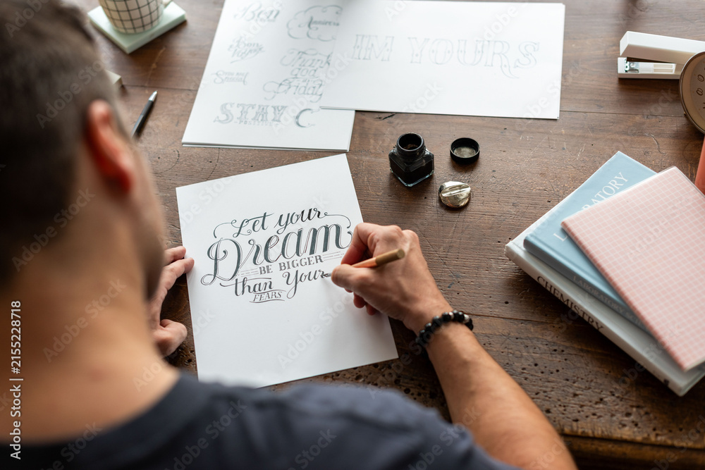 Obraz premium Person practicing calligraphy at a wooden desk with ink and paper.