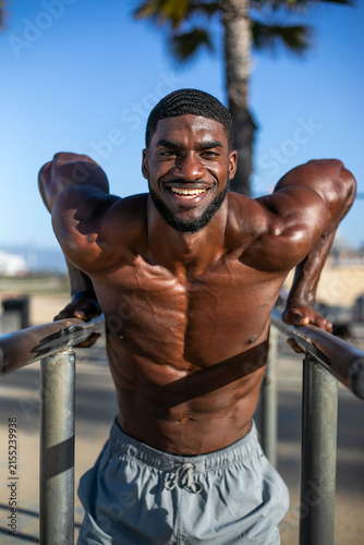 Quadro su tela Man exercising outdoors on parallel bars, smiling under a clear sky